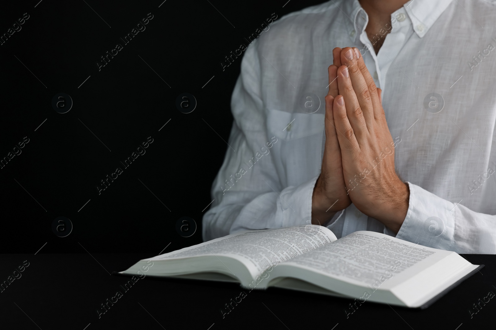 Photo of Man with Bible praying at black table, closeup