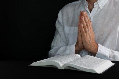 Photo of Man with Bible praying at black table, closeup