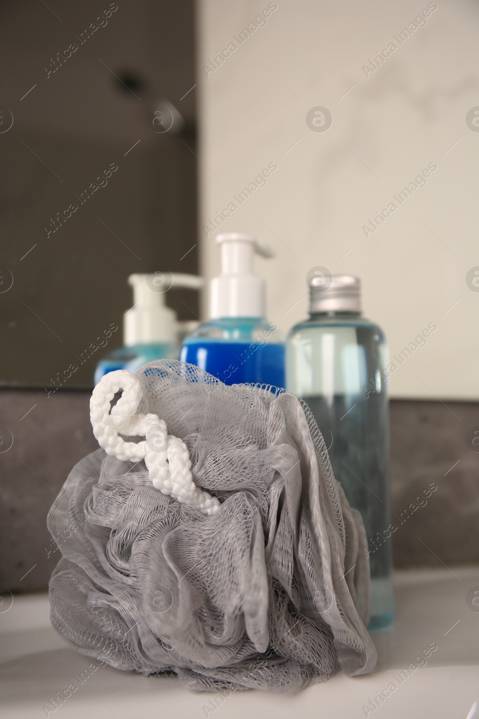 Photo of Grey shower puff and cosmetic products on washbasin in bathroom