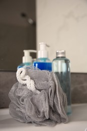 Grey shower puff and cosmetic products on washbasin in bathroom