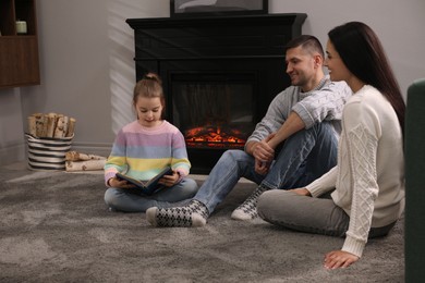 Photo of Happy family reading book together on floor near fireplace at home
