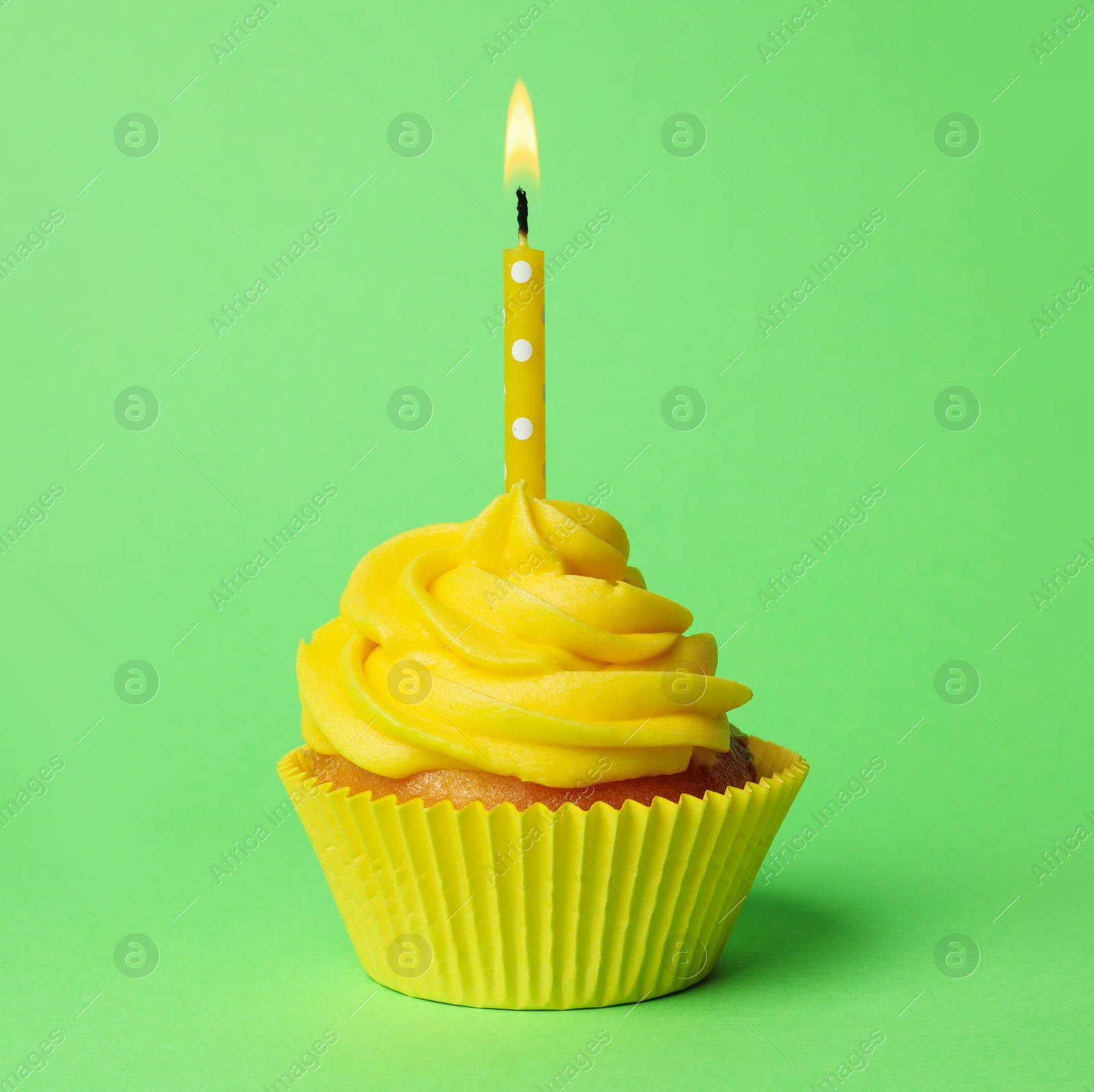 Photo of Delicious birthday cupcake with yellow cream and burning candle on green background