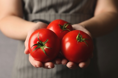 Woman with ripe tomatoes on grey background, closeup