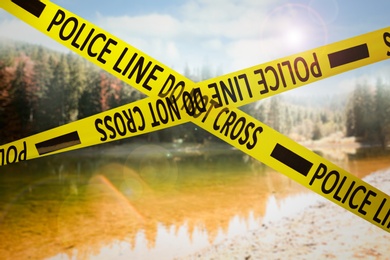 Yellow police tape isolating crime scene. Blurred view of mountain lake
