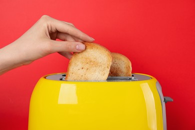 Woman taking bread slice out of toaster on red background, closeup