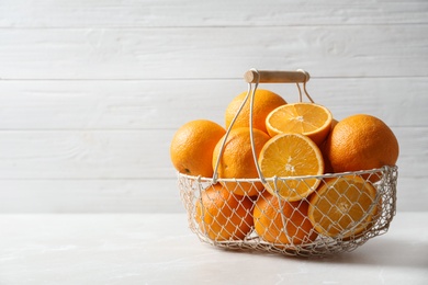 Photo of Basket with ripe oranges on table against light background. Space for text