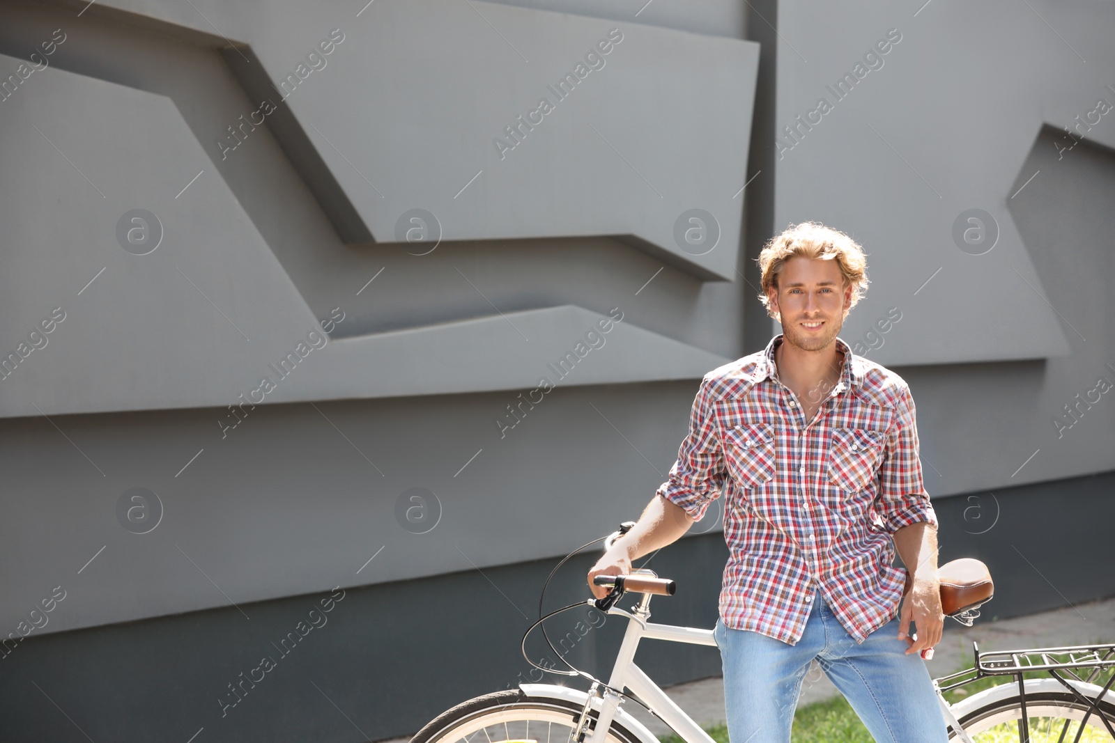 Photo of Handsome young man with bicycle near gray wall outdoors. Space for text