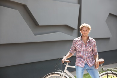 Photo of Handsome young man with bicycle near gray wall outdoors. Space for text
