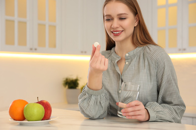 Young woman with glass of water and vitamin pill at table in kitchen