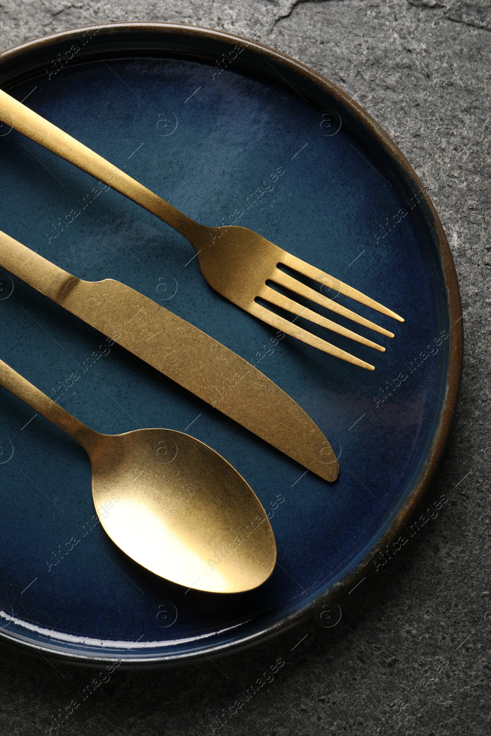 Photo of Stylish golden cutlery and plate on grey table, top view