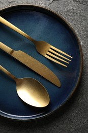 Stylish golden cutlery and plate on grey table, top view