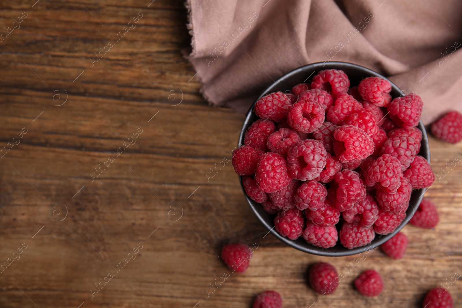 Photo of Bowl with fresh red ripe raspberries on wooden table, flat lay. Space for text