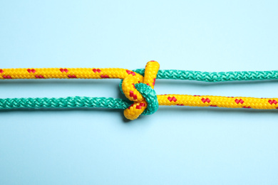 Photo of Colorful ropes with knot on light blue background, top view. Unity concept