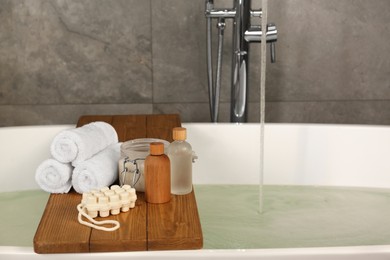 Photo of Wooden tray with spa products and towels on bath tub in bathroom