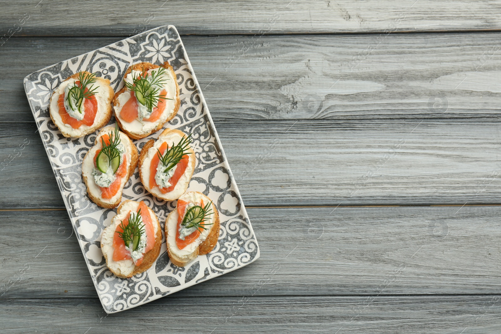 Photo of Tasty canapes with salmon, cucumber, cream cheese and dill on wooden table, top view. Space for text