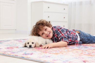 Photo of Little boy lying with cute puppy on carpet at home