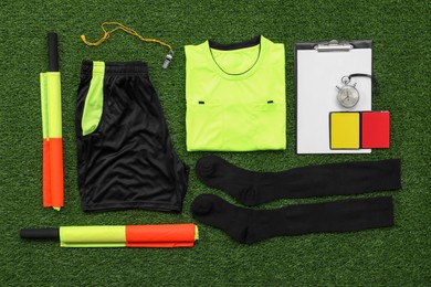 Photo of Uniform and other referee equipment on green grass, flat lay
