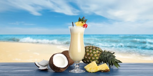 Image of Tasty Pina Colada cocktail on blue wooden table near ocean. Banner design