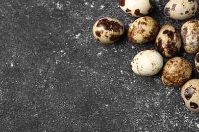 Photo of Many speckled quail eggs on black textured table, flat lay. Space for text