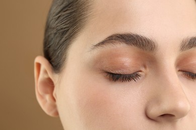 Photo of Young woman with perfect eyebrows on brown background, closeup