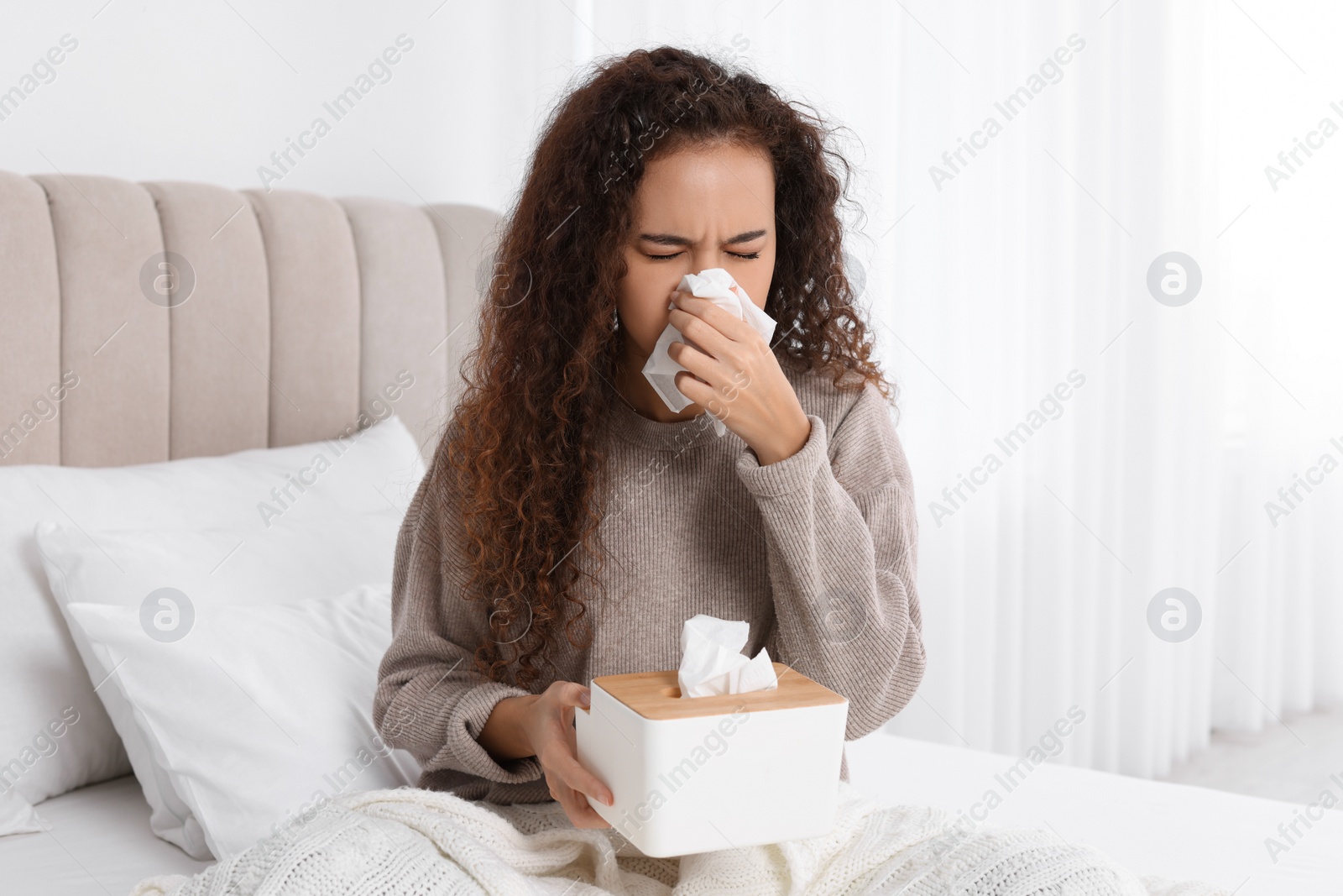 Photo of Sick African American woman with box of paper tissues suffering from cold in bed at home