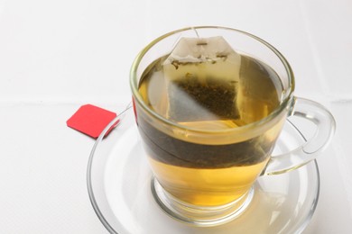 Photo of Tea bag in cup with hot drink on white table, closeup