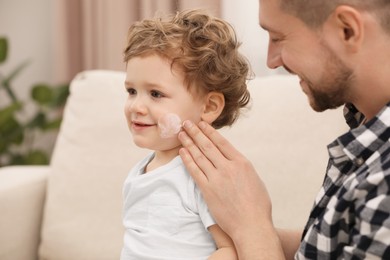 Photo of Father applying ointment onto his son`s cheek on sofa at home
