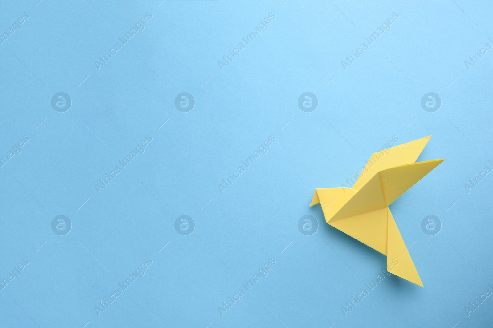 Photo of Origami art. Beautiful handmade paper bird on light blue background, top view. Space for text