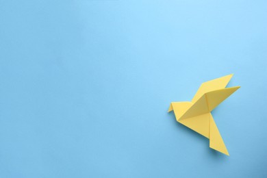 Photo of Origami art. Beautiful handmade paper bird on light blue background, top view. Space for text