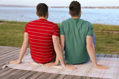 Photo of Gay couple sitting near river on sunny day, back view