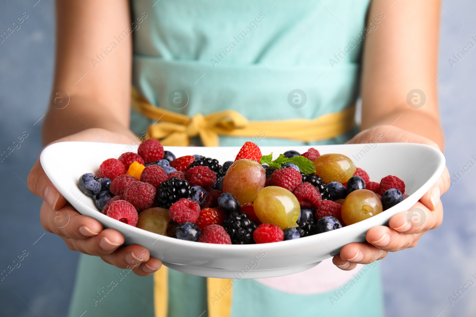 Photo of Woman holding plate of fresh tasty fruit salad against blue background, closeup