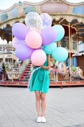 Photo of Young woman hiding behind color balloons near carousel