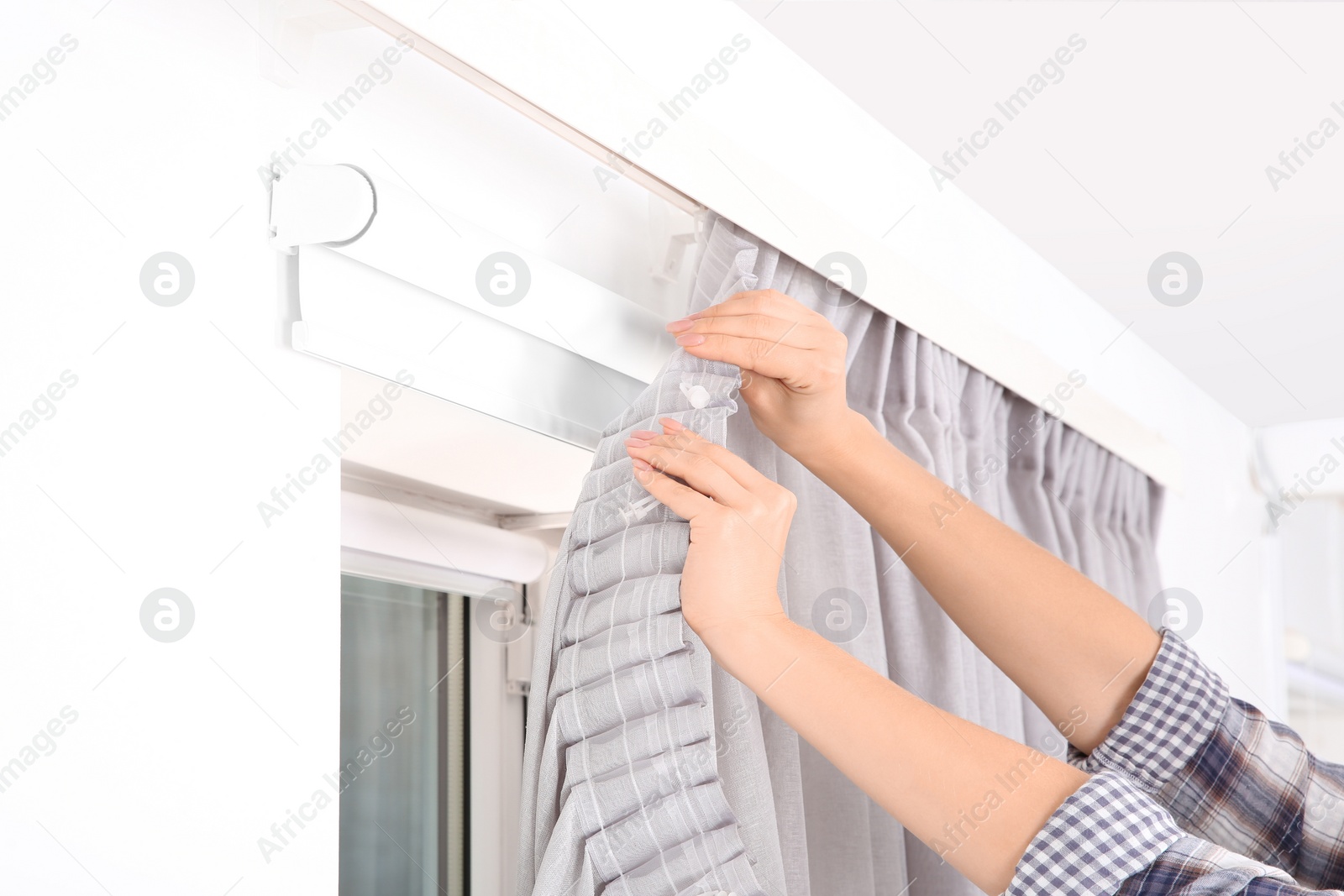 Photo of Woman hanging window curtain indoors, closeup. Interior decor element