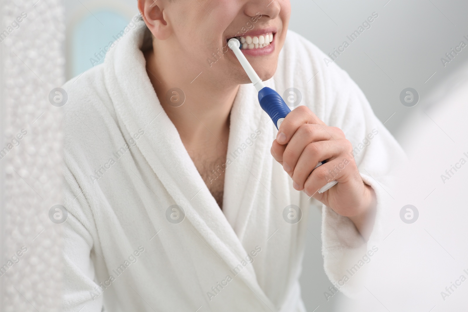 Photo of Man brushing his teeth with electric toothbrush near mirror, closeup