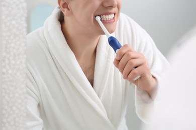 Photo of Man brushing his teeth with electric toothbrush near mirror, closeup
