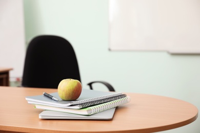 Photo of Stack of books, apple and laptop on teacher's desk in classroom