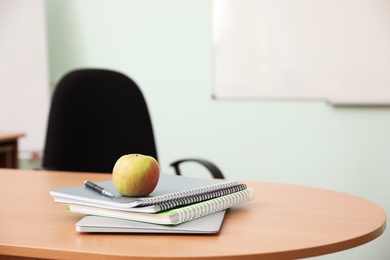 Stack of books, apple and laptop on teacher's desk in classroom