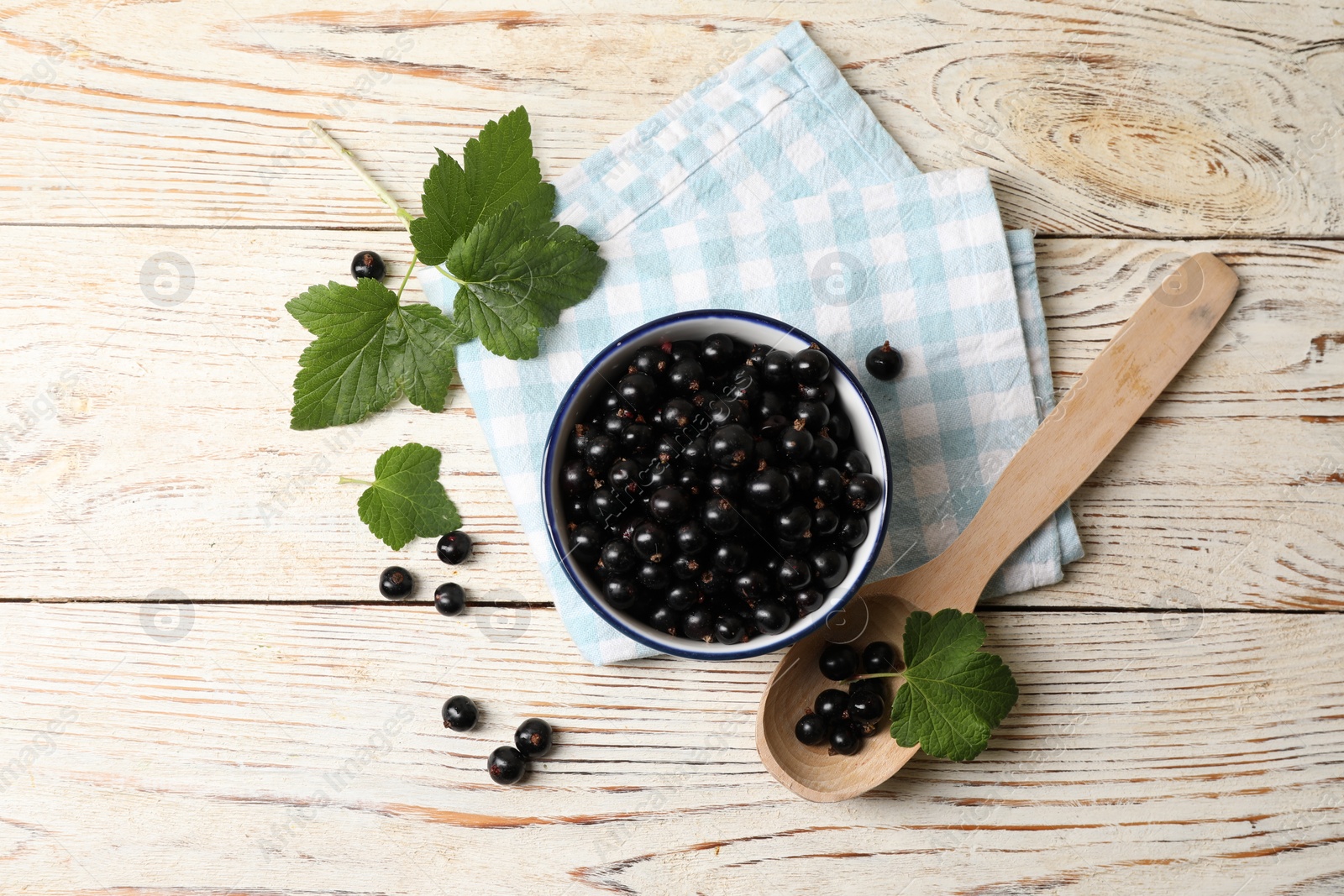 Photo of Ripe blackcurrants and leaves on light wooden table, flat lay