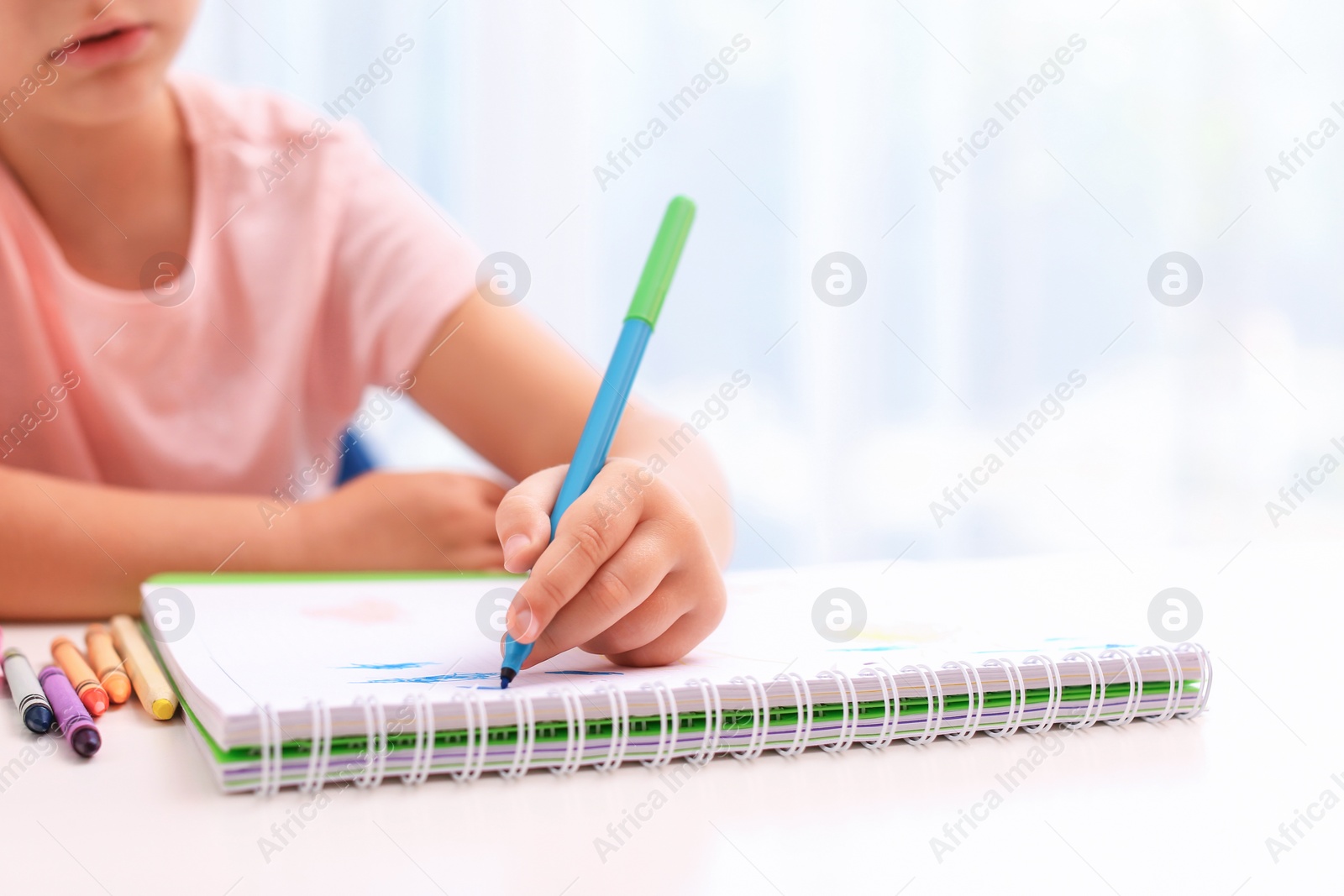 Photo of Little left-handed girl drawing at table in room, closeup