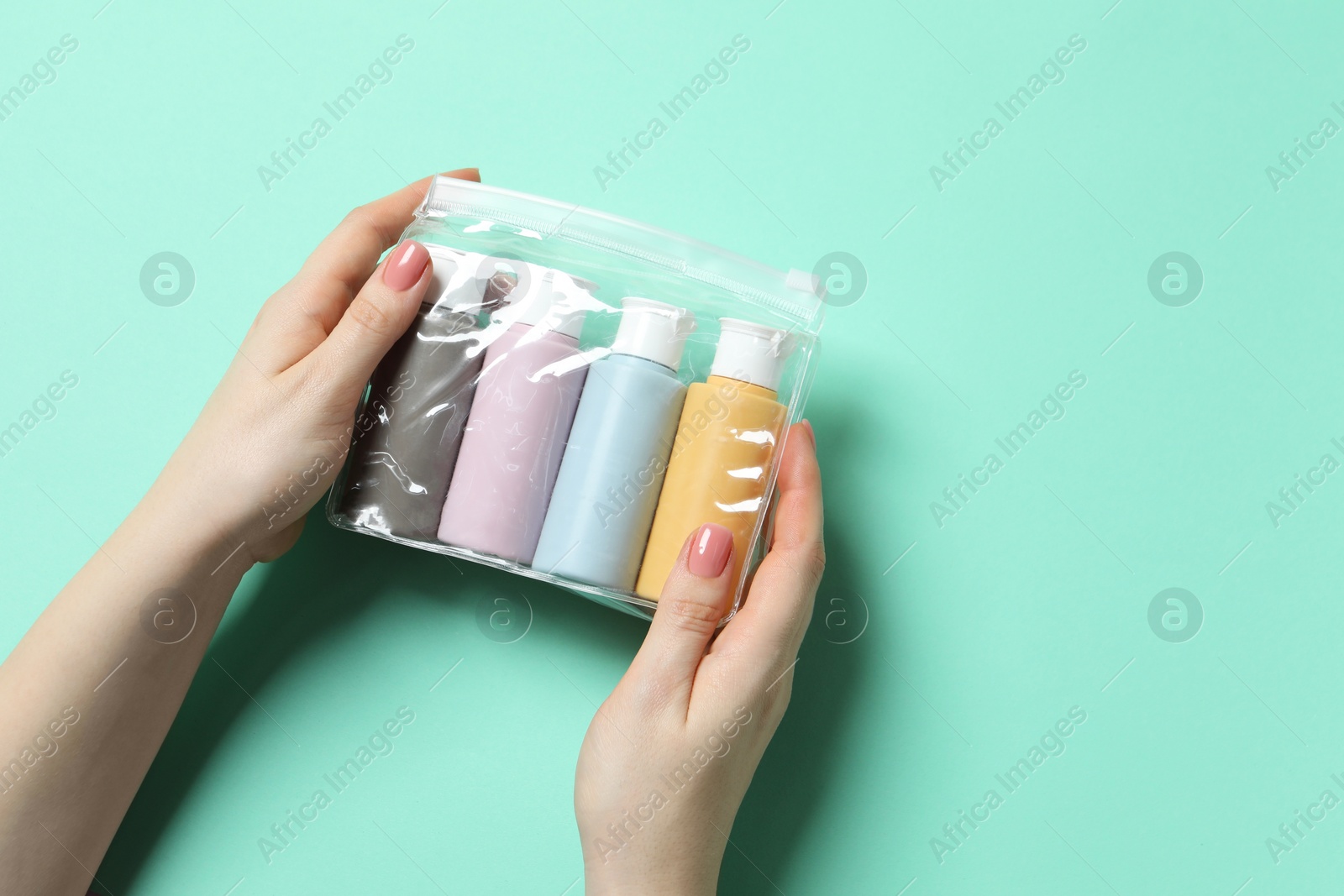 Photo of Cosmetic travel kit. Woman holding plastic bag with small bottles of personal care products against turquoise background, top view. Space for text