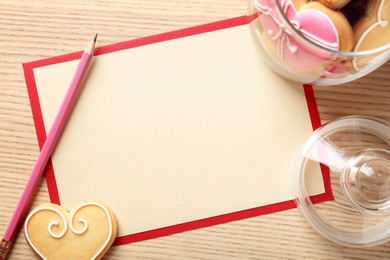 Photo of Flat lay composition with heart shaped cookies and blank card on wooden background, space for text