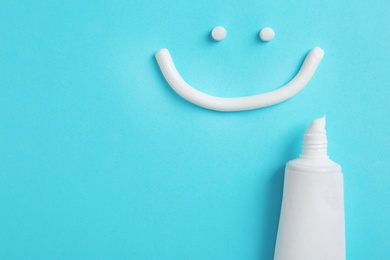 Photo of Smiling face made of toothpaste, tube and space for text on color background, top view