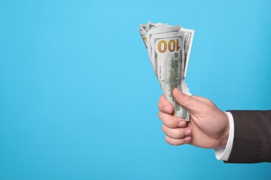 Photo of Man holding money on light blue background, closeup. Space for text. Currency exchange