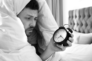 Image of Sleepy man with alarm clock at home in morning. Black and white photography