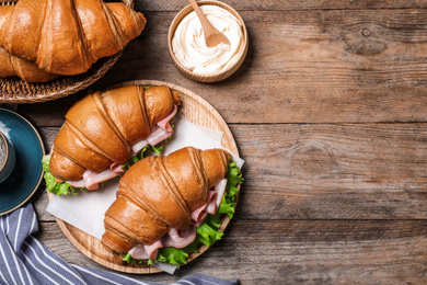 Tasty croissant sandwiches with ham on wooden table, flat lay. Space for text