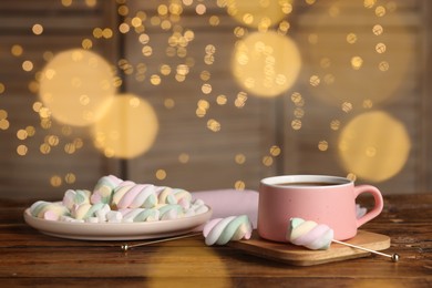 Photo of Cup of delicious hot chocolate and marshmallows on wooden table against festive lights