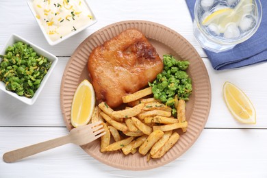 Photo of Tasty fish, chips, sauce, peas and lemon on white wooden table, top view