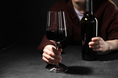 Photo of Alcohol addiction. Woman with red wine at dark textured table, selective focus