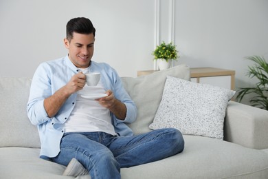 Man with cup of drink sitting on comfortable sofa in living room