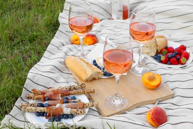 Photo of Glasses of delicious rose wine and food on picnic blanket outdoors